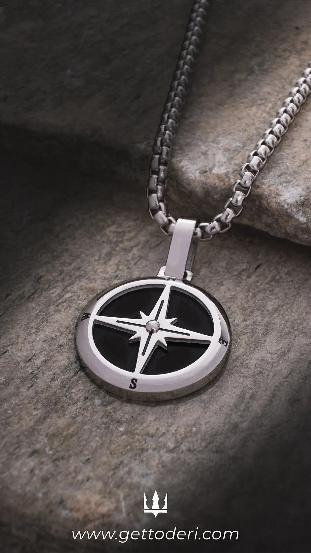 Gümüş renkli pusula desenli metal kolye, siyah detaylı, taş zeminde