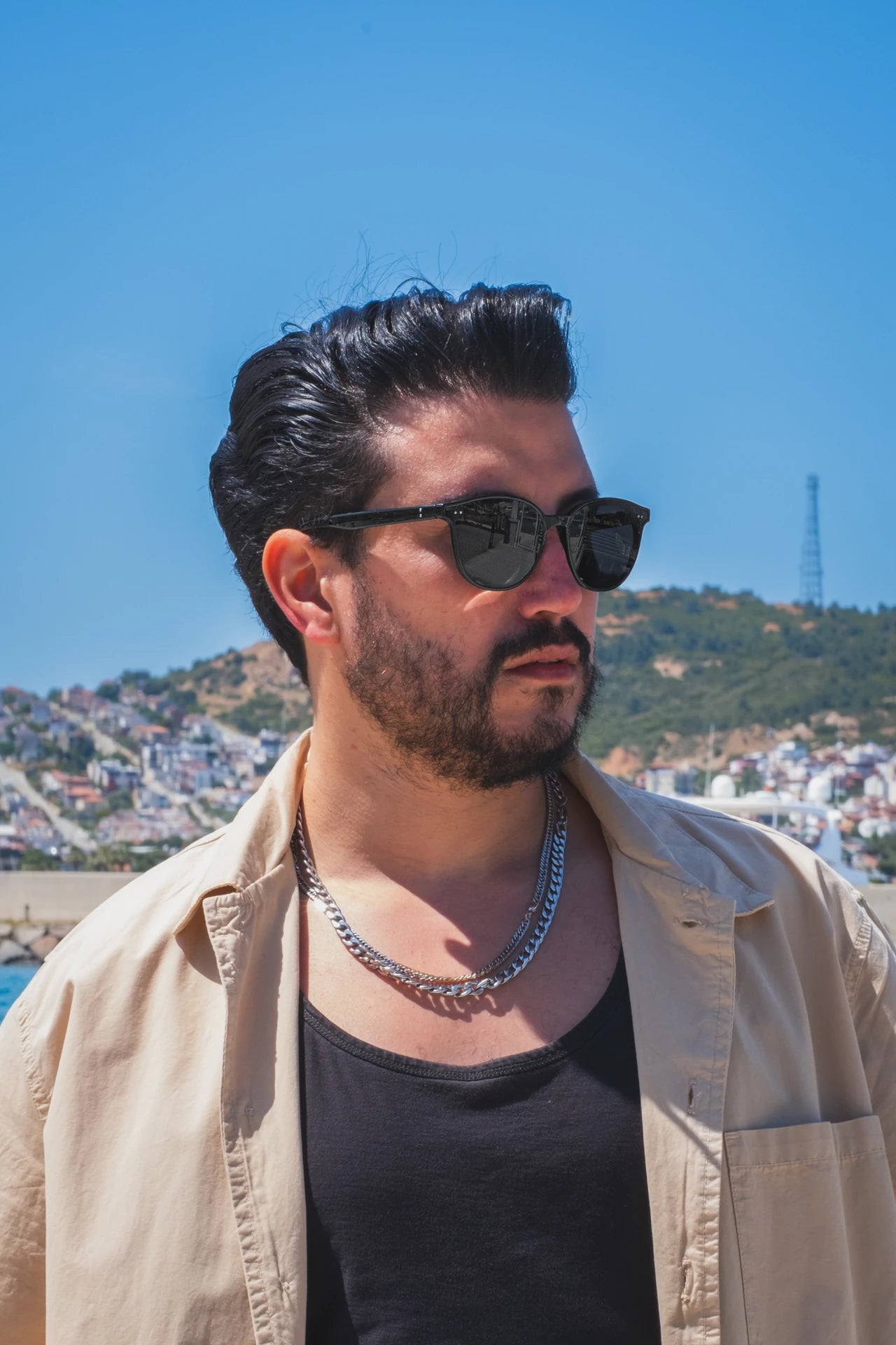 Siyah güneş gözlüğü takan adam, açık mavi gökyüzü ve dağlı manzara önünde