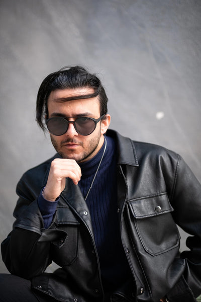 Siyah deri ceket giyen erkek model, koyu mavi yün turtleneck ve güneş gözlüğüyle stil sahibi görünüm.