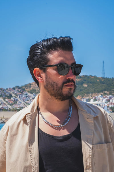 Siyah güneş gözlüğü takan adam, açık mavi gökyüzü ve dağ manzarası önünde